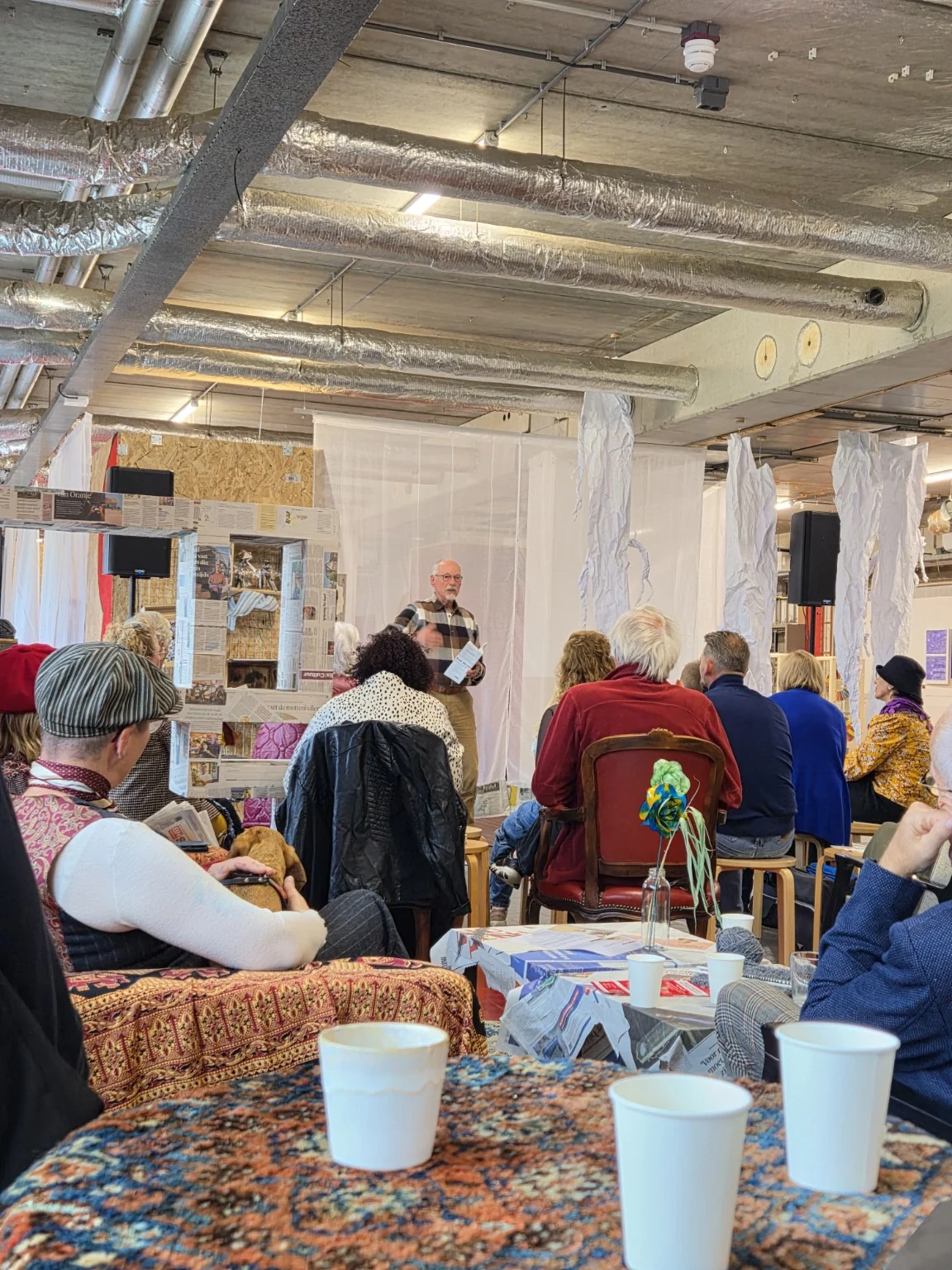 Luisteraars tussen de kunstwerken, met een voordrager bij de microfoon op de achtergrond